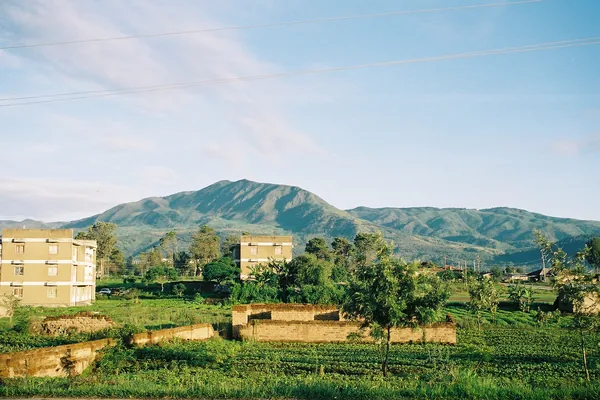 Majengo na mashamba Mbeya na milima ya kijani nyuma.