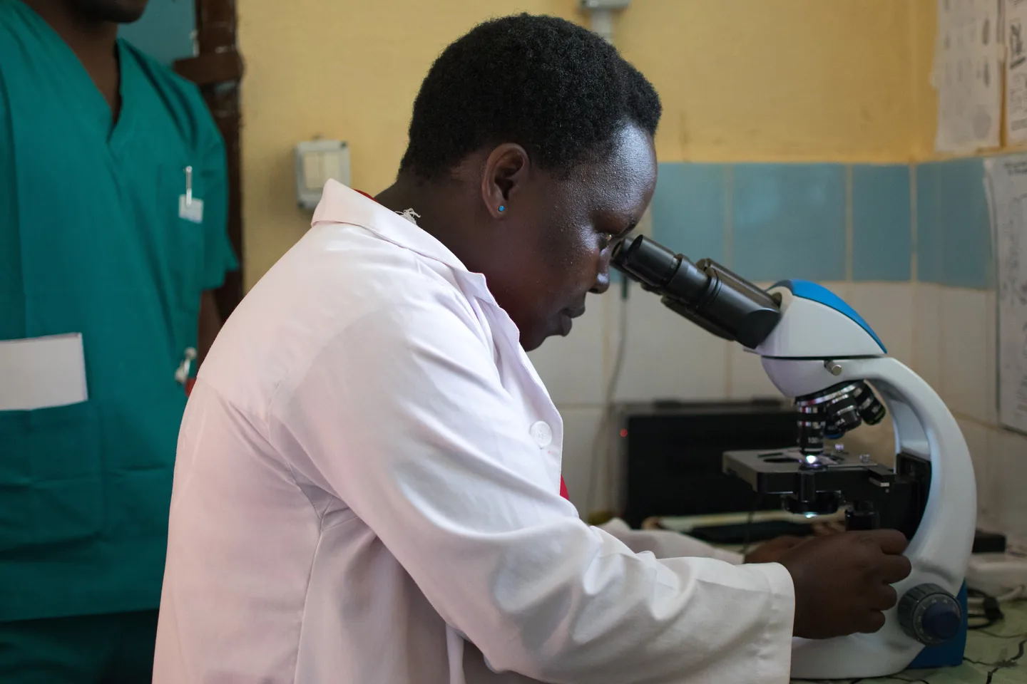 Mtaalamu wa maabara aliyevaa koti jeupe akitazama kwenye hadubini nchini Tanzania.