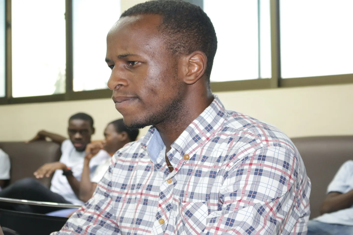 A young man in a checked shirt listening closely in a room in Dar es Salaam.