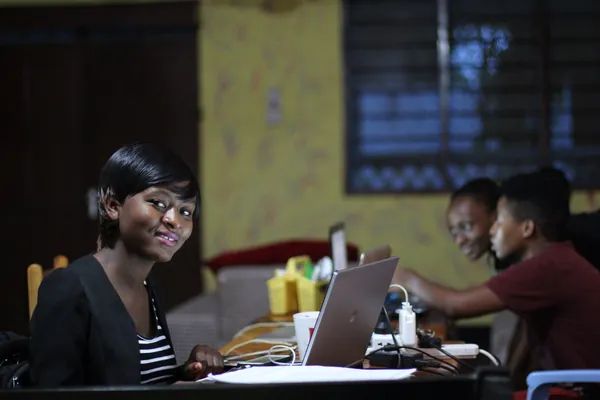 A young woman smiling at a laptop in a shared workspace in Tanzania.