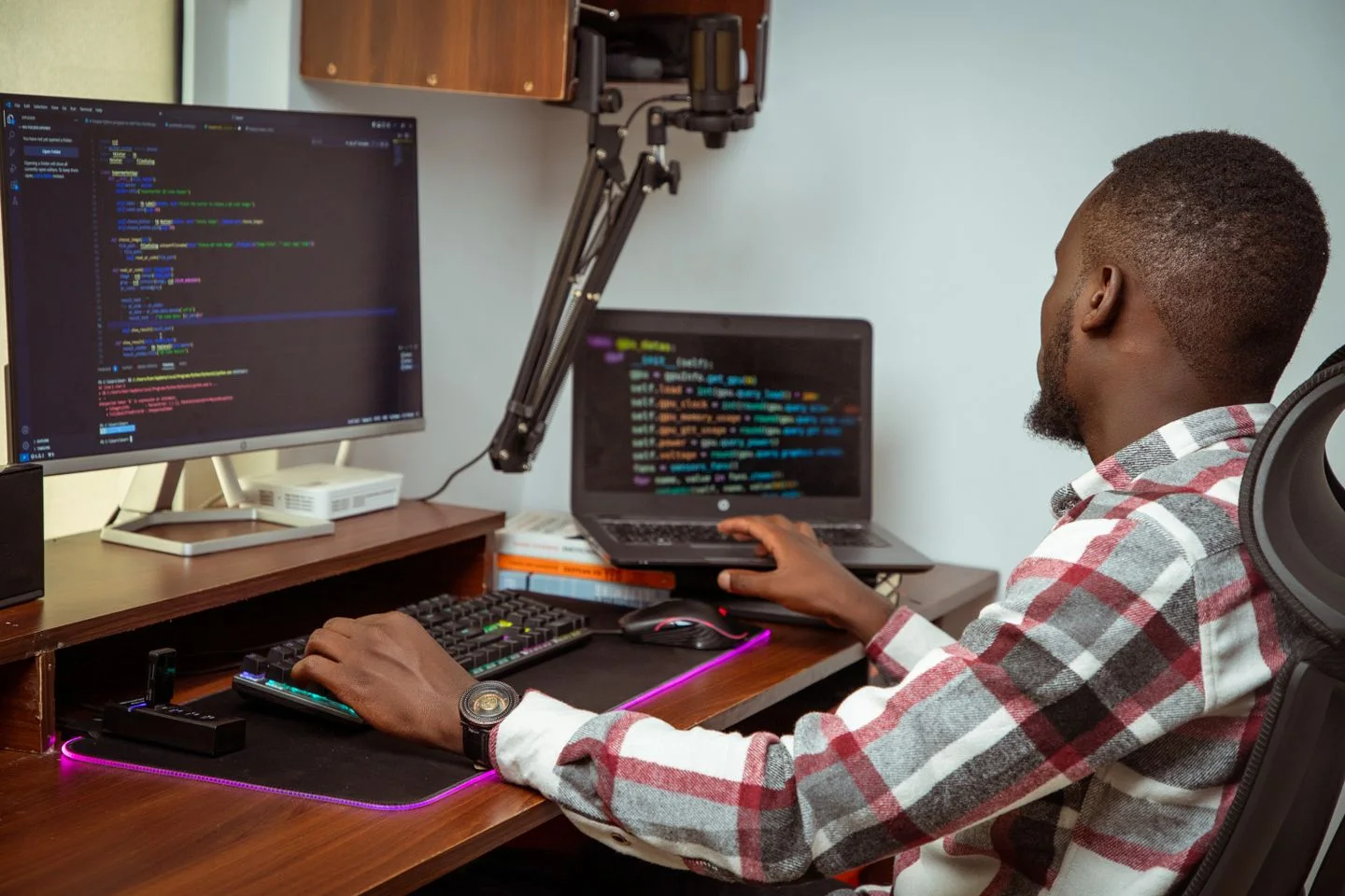 A developer writes code on a desktop computer and a laptop in a Nairobi office.