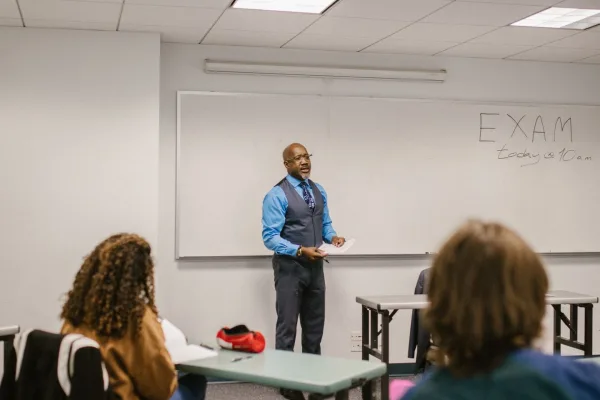 A lecturer speaks to students in front of a whiteboard.