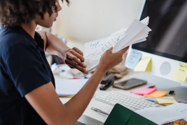 An office worker sorts papers at her desk beside a computer.
