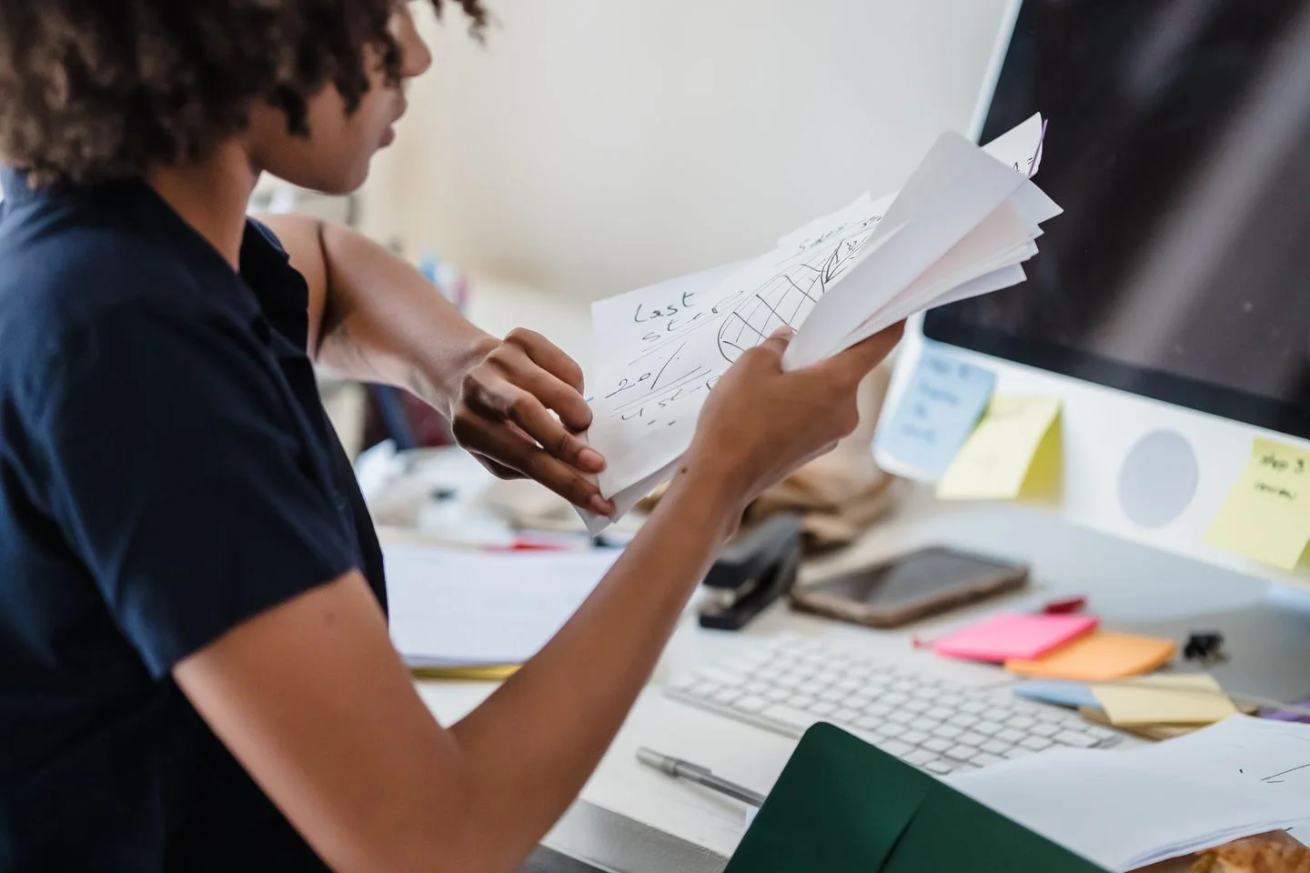 An office worker sorts papers at her desk beside a computer.