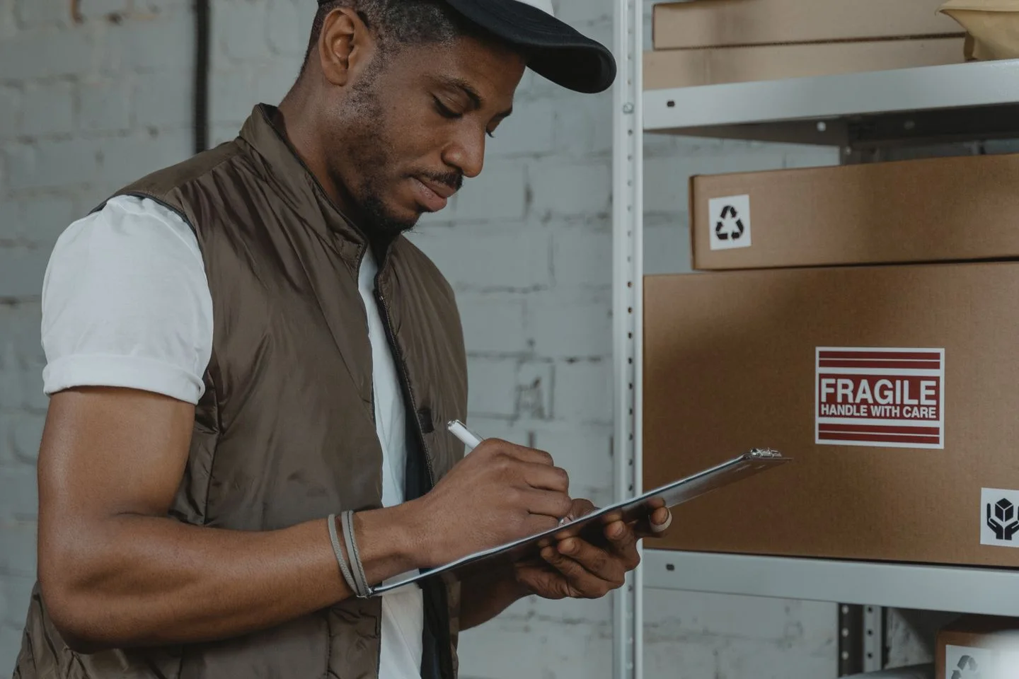 A storekeeper writes on a clipboard beside shelves of boxes.